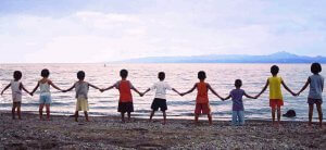 A group of children stand hand in hand on a beach in the Philippines.